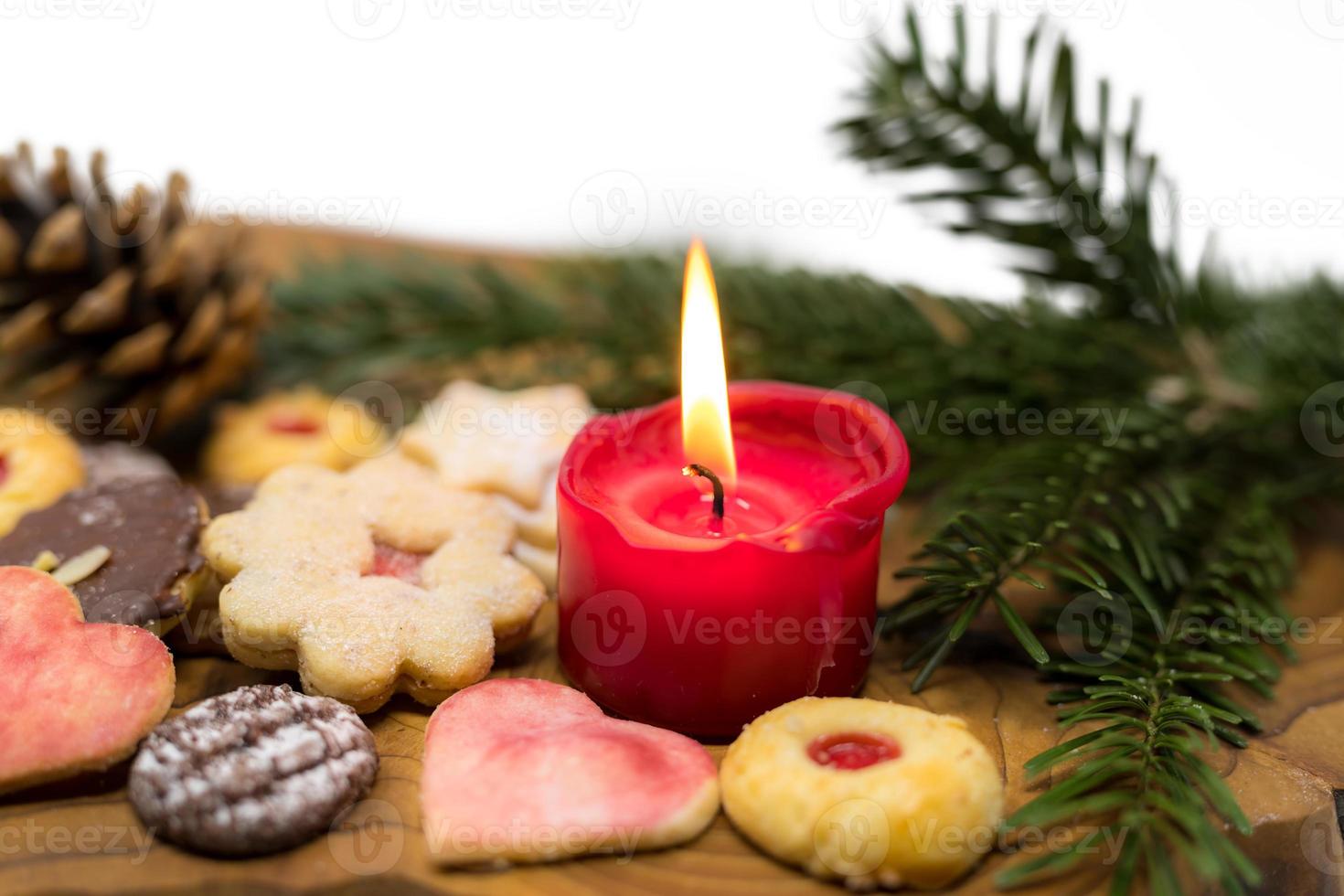 brinnande rött ljus står mellan dekorerade julkakor på en träskiva foto