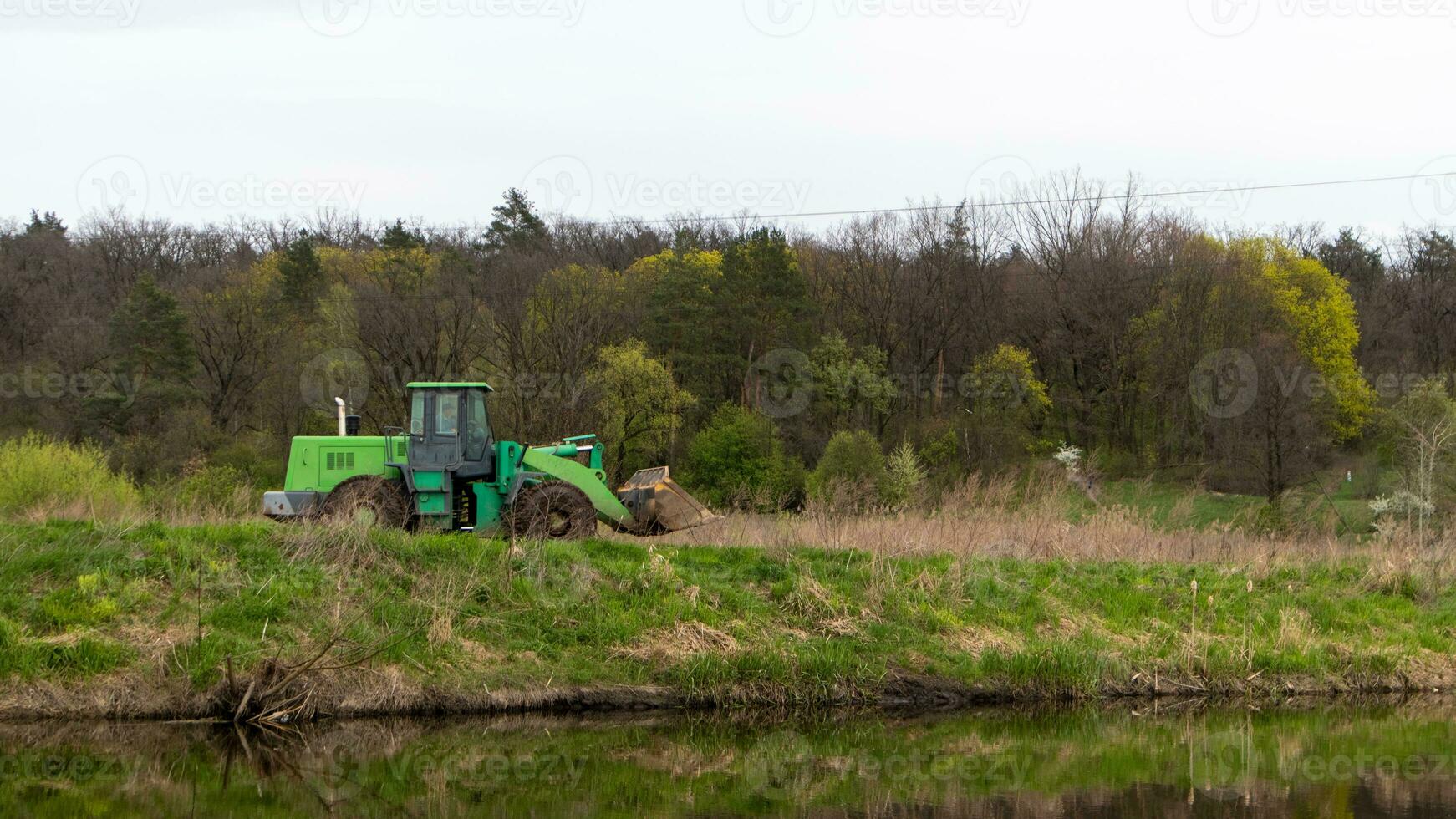 de traktor rider längs de Bank av en flod eller sjö i de skog. foto