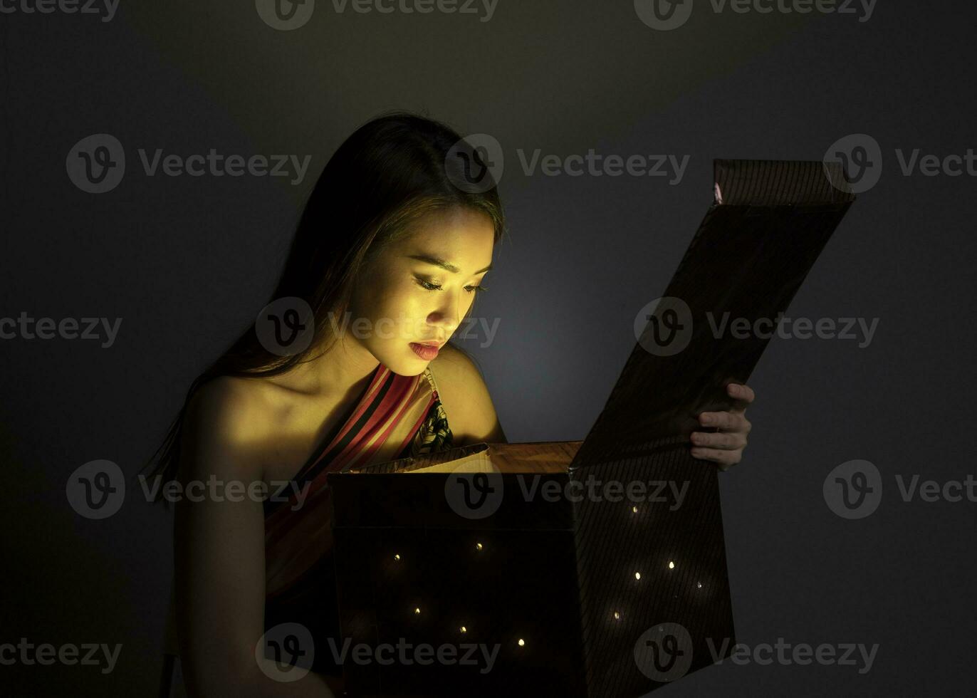 asiatisk kvinna öppning mystiker bok låda magisk ljus mörk bakgrund foto