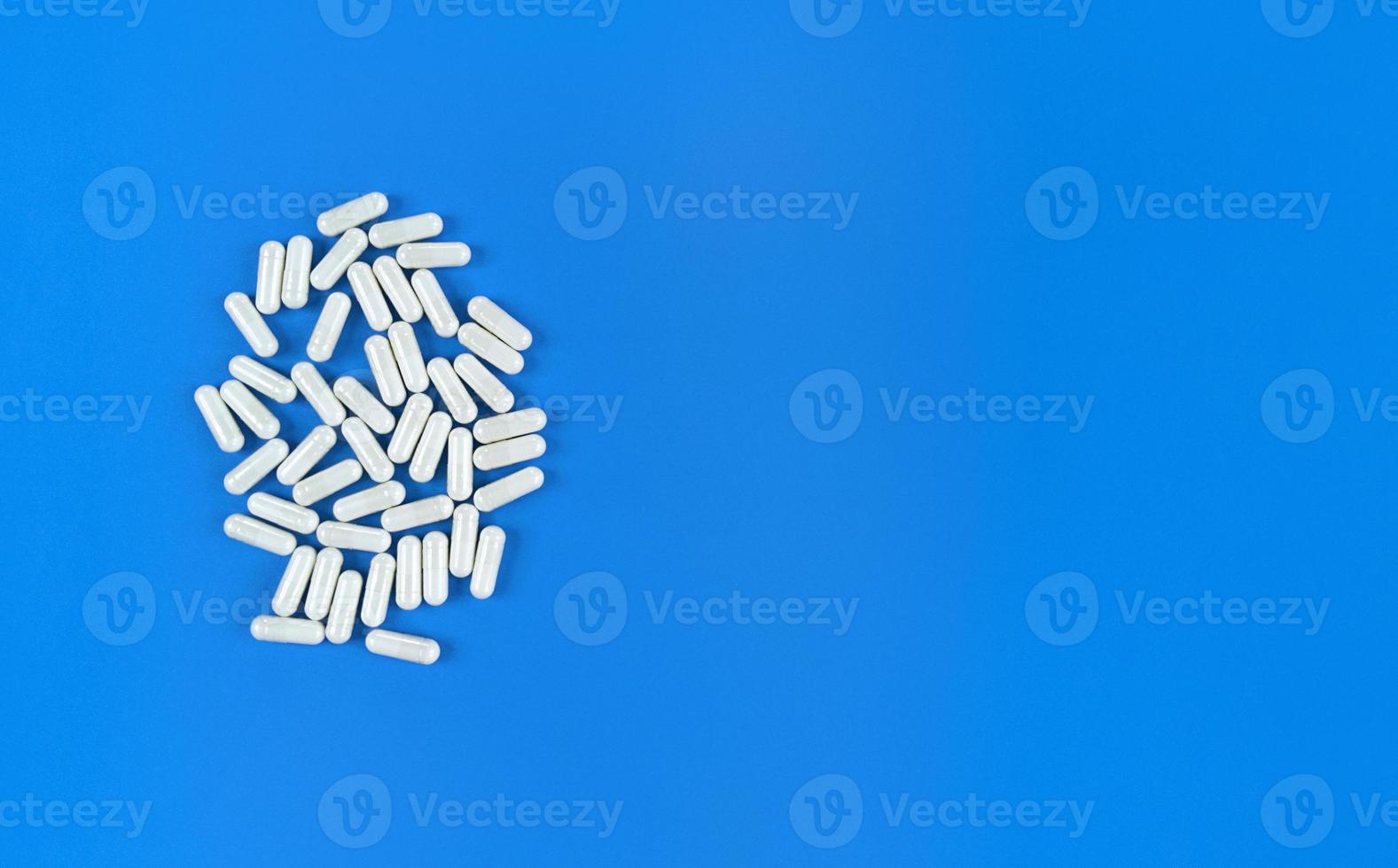 vita spridda piller kapslar på blå bakgrund med kopia utrymme foto