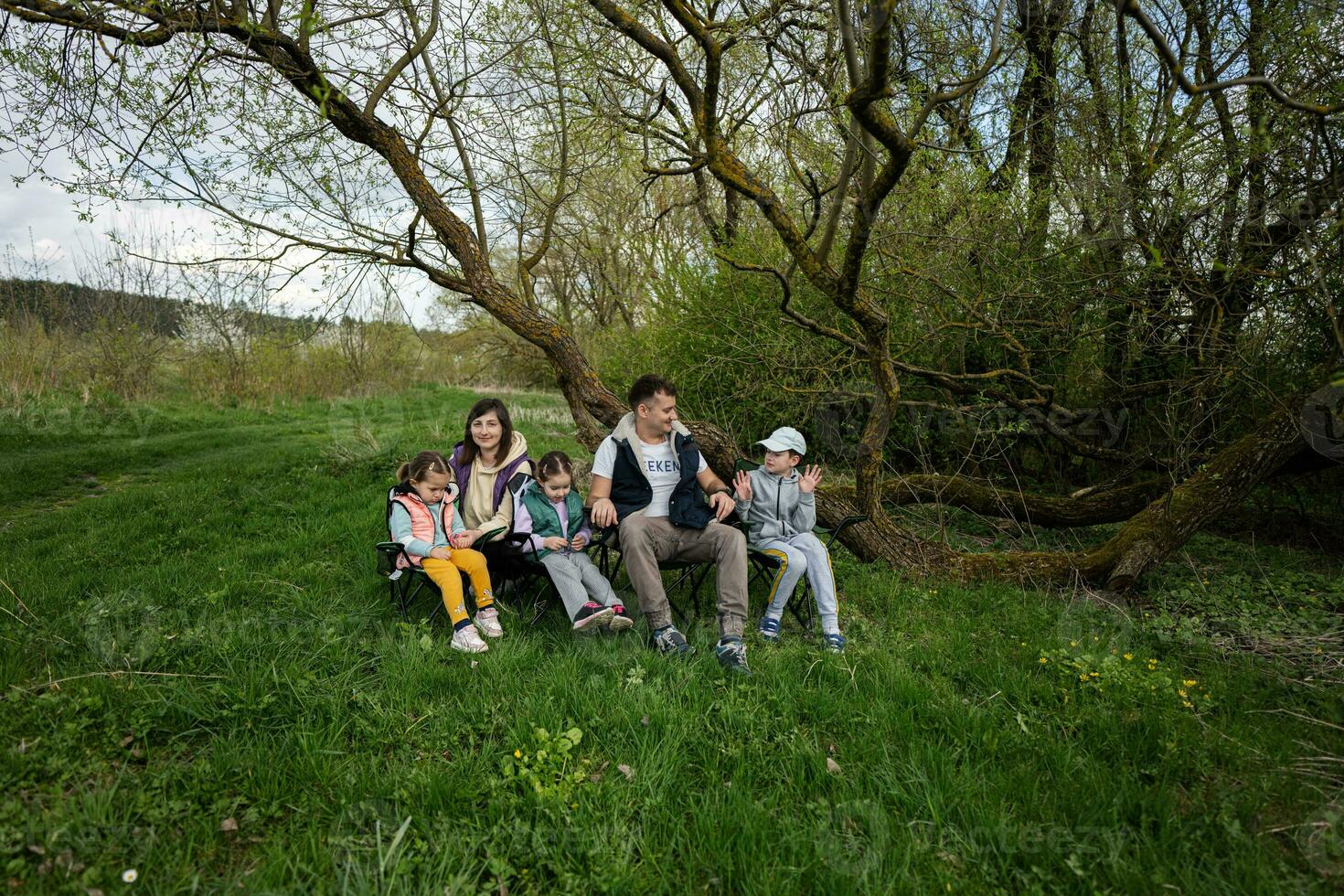 familj med tre barn Sammanträde på stolar på vår skog. foto