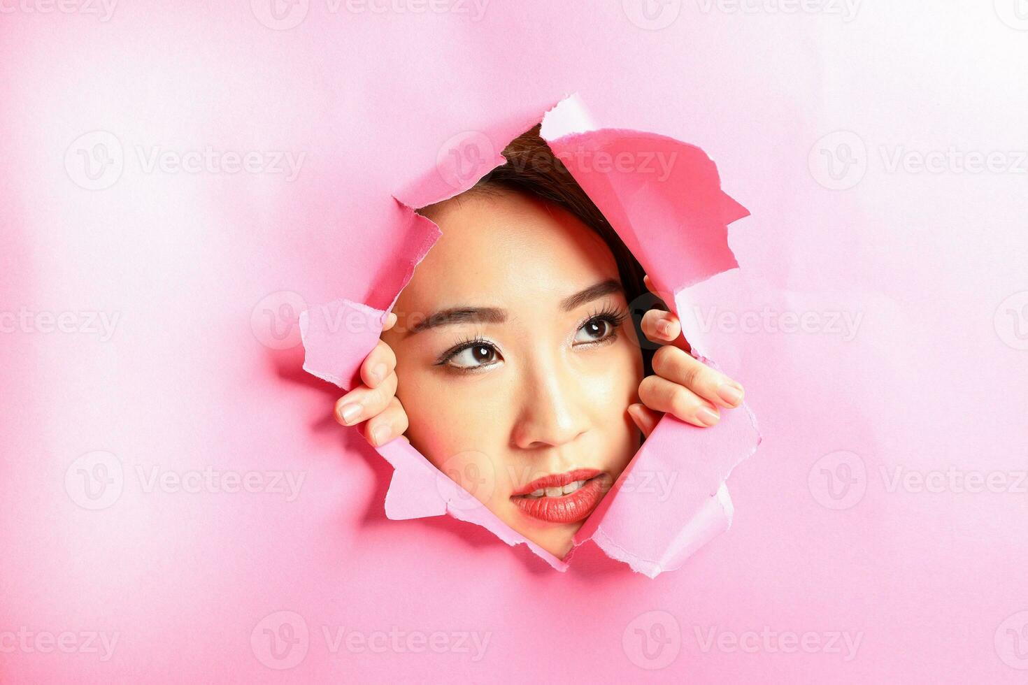 ung skön asiatisk kvinna uttryck genom trasig papper hål foto