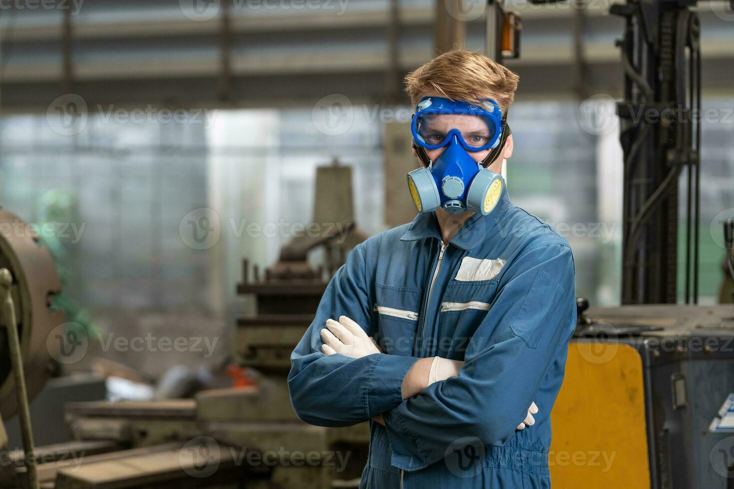 nödsituation förorening fabrik begrepp. porträtt ingenjör bär en mekanisk overall och gas mask ser på de kamera med hans vapen korsade. foto