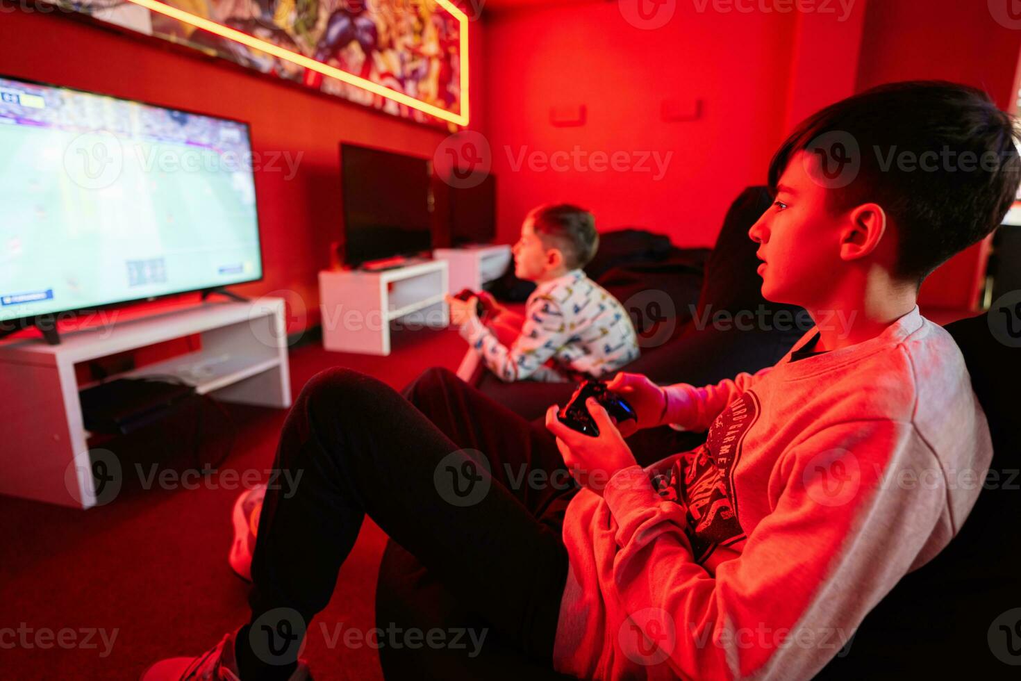 två Pojkar spelare spela fotboll gamepad video spel trösta i röd gaming rum. foto