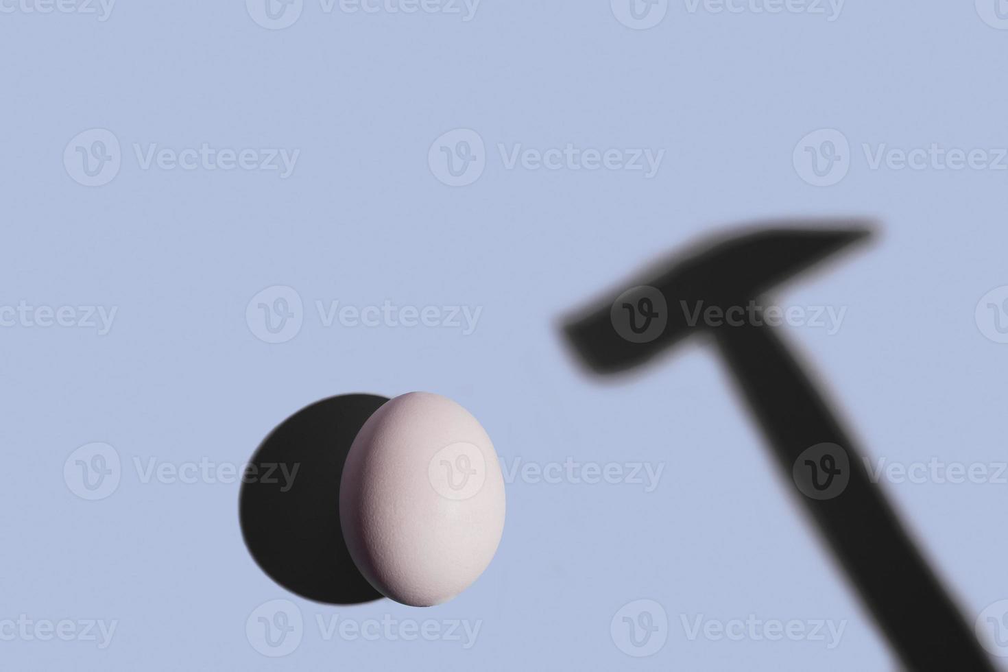 minimalt koncept med ett ägg under det hårda ljuset och en hammerskugga på blå bakgrund foto