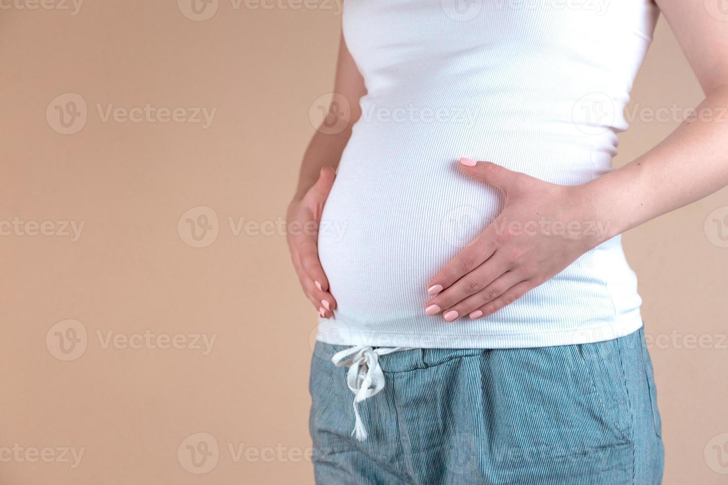 äkta närbild av en ung gravid kvinna i pyjamas som smeker hennes mage foto