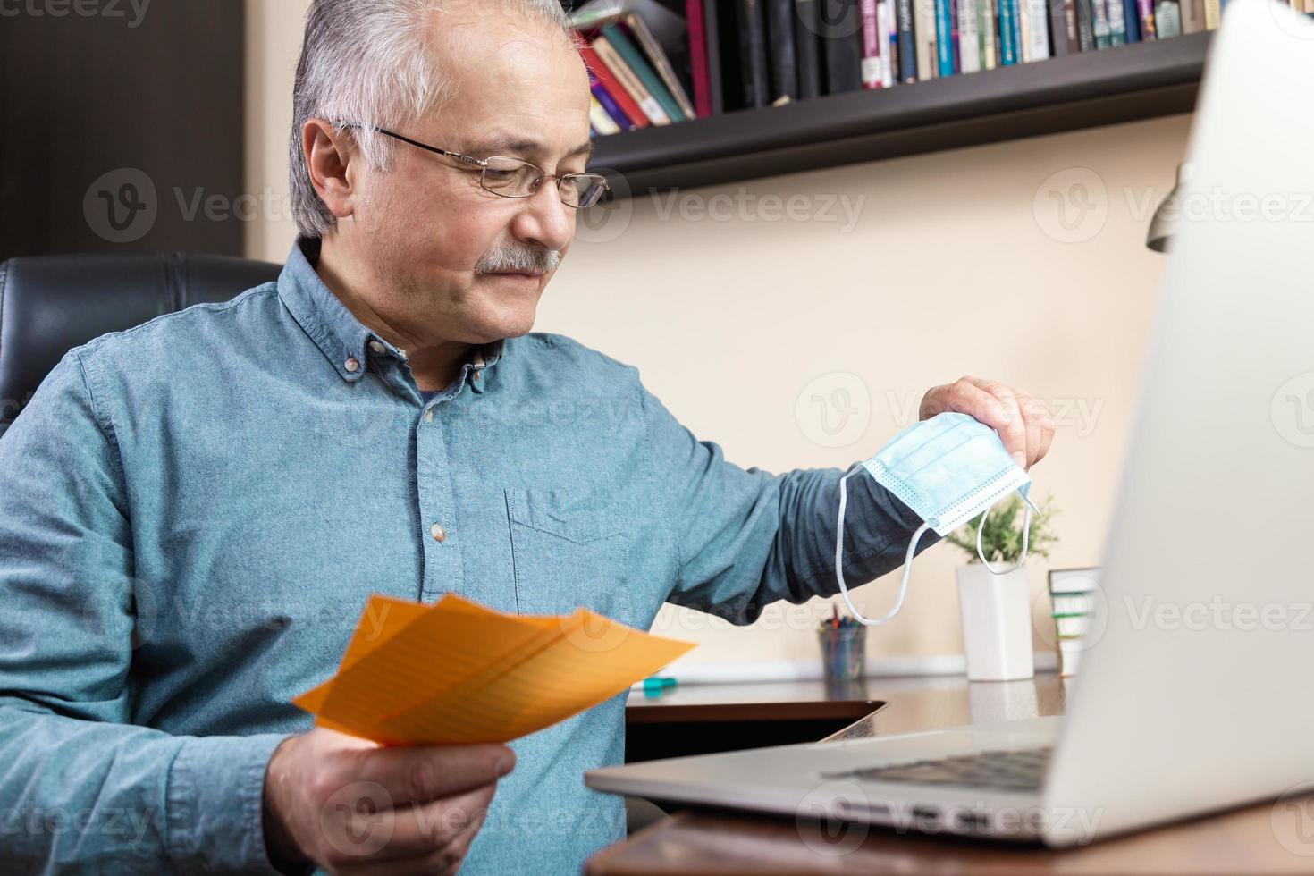 äldre man som hemma arbetar med bärbar dator som surfar räkningar och dokument foto