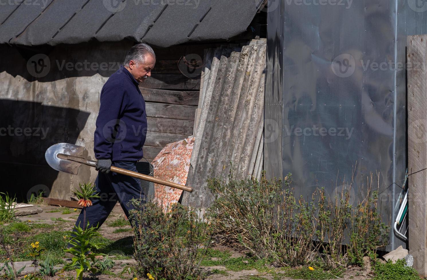 vuxen manlig bonde bär en spade i sin trädgård foto