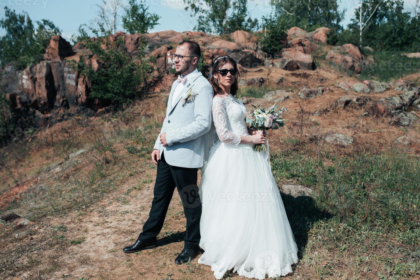 bröllopsfotografering moderiktiga bruden och brudgummen i solglasögon på naturen på klipporna foto