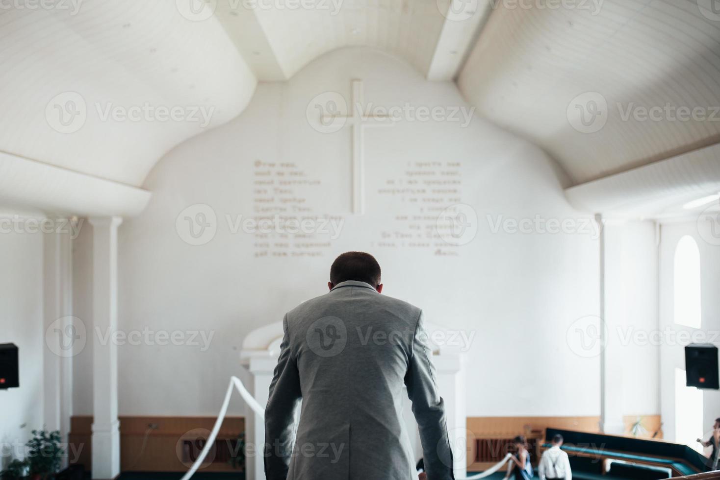 bröllopsfoto av känslor av en skäggig brudgum med glasögon i en grå jacka i kyrkan foto