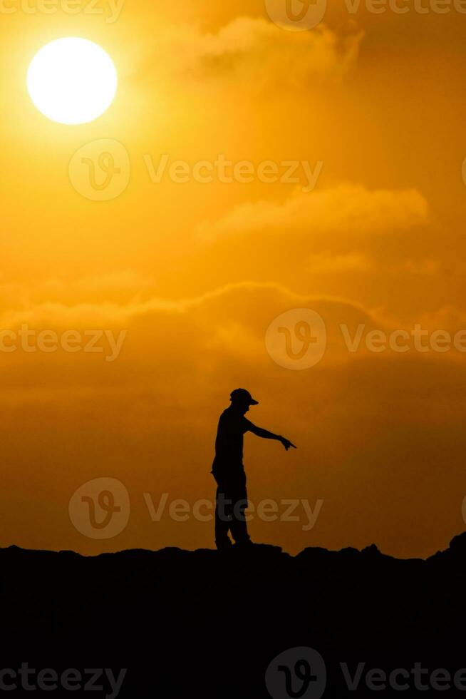 silhuett av två män på en skön orange solnedgång. ponting på något på solnedgång foto