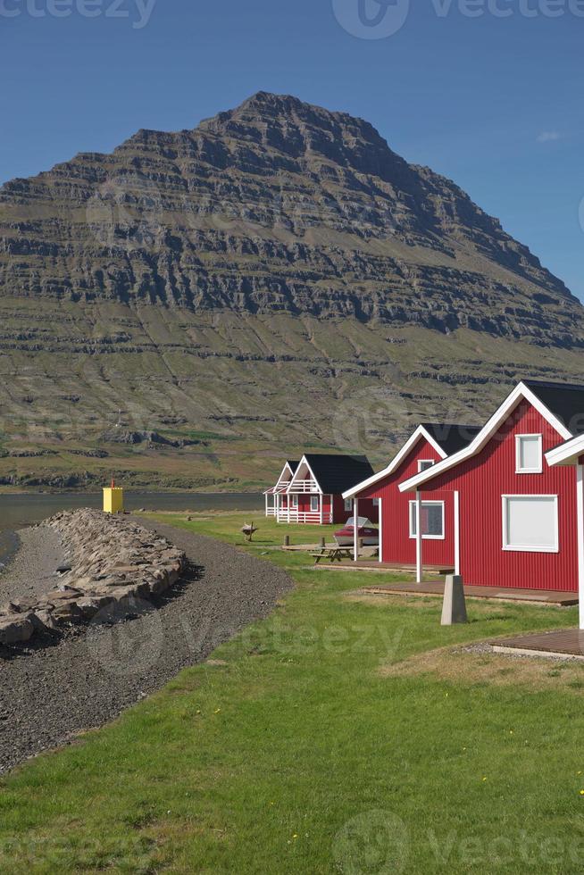 traditionellt rött målat träpanelhus med mäktigt holmatindurberg i bakgrunden i eskifjordur östra Island foto