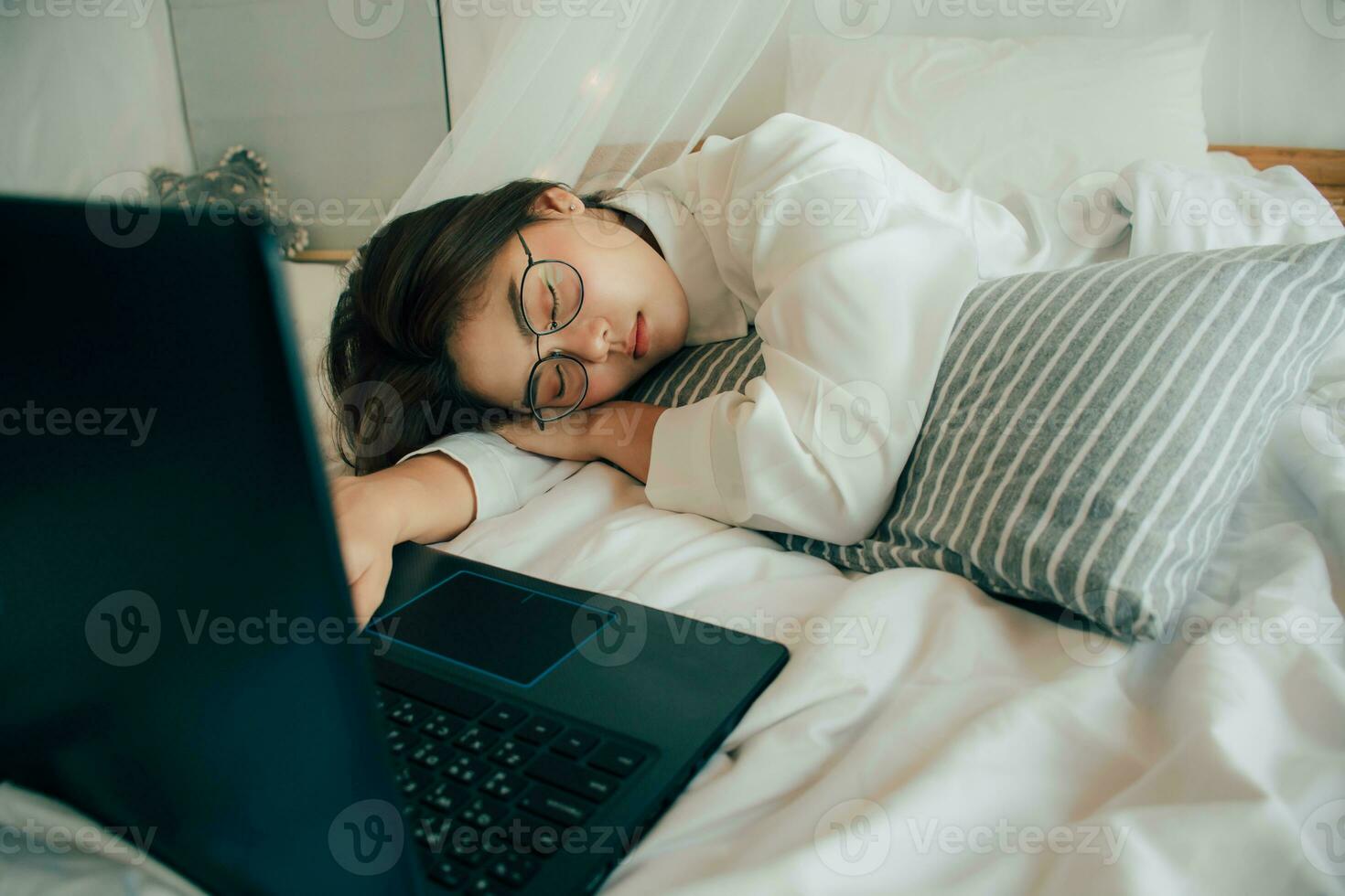 skön asiatisk flicka i vit pyjamas sover på de säng med bärbar dator på Hem. överarbetad affärskvinna sovande över en dator. ung trött kvinna falla sovande. människor och livsstil begrepp. foto