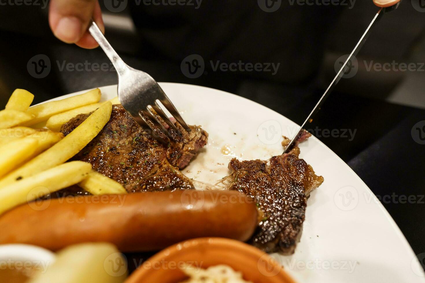 man äter grillad kött insats från tallrik. hand innehav kniv och gaffel skärande grillad nötkött biff foto