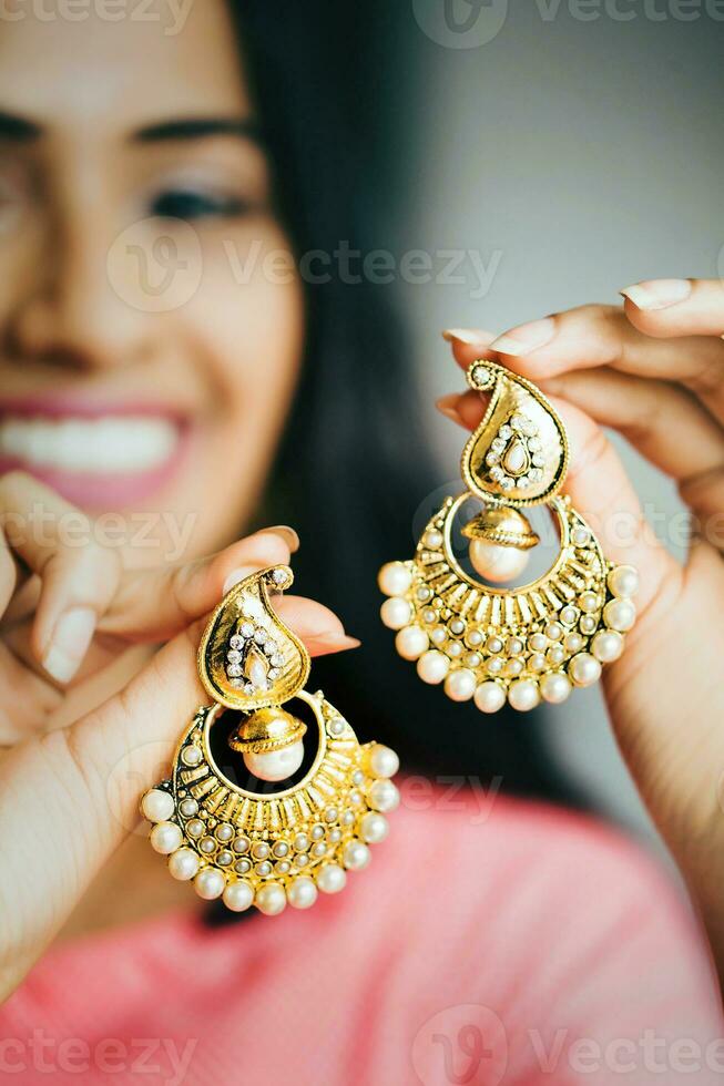 ung skön indisk innehav en par av guld och diamant örhängen foto