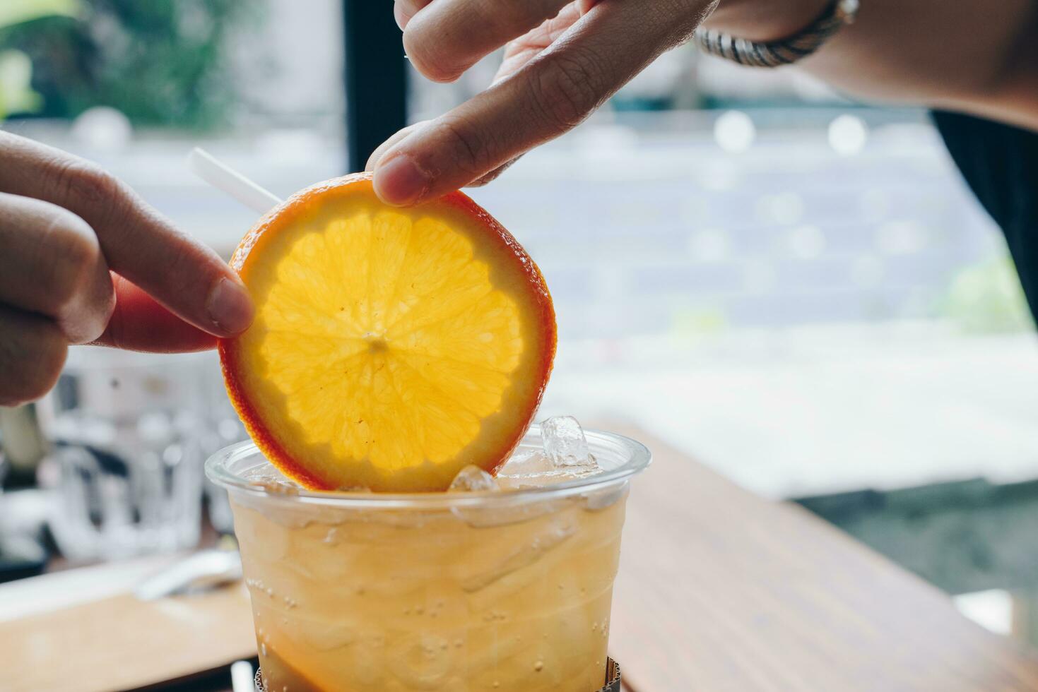 stänga upp av mänsklig händer innehav en bit av orange på en glas kopp av orange juice. foto