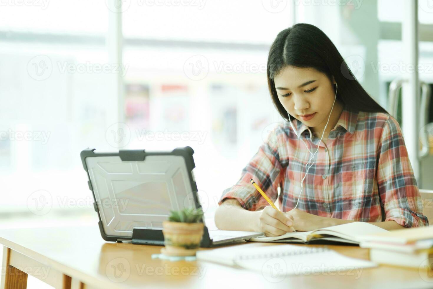 ung asiatisk kvinna studie i främre av de bärbar dator dator och och använder sig av hörlurar på utanför platsen. foto