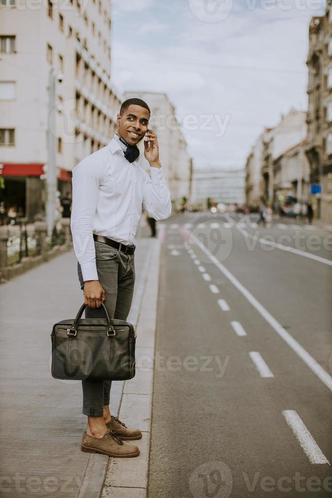 ung afroamerikansk affärsman som använder en mobiltelefon medan han väntar på en taxi på en gata foto