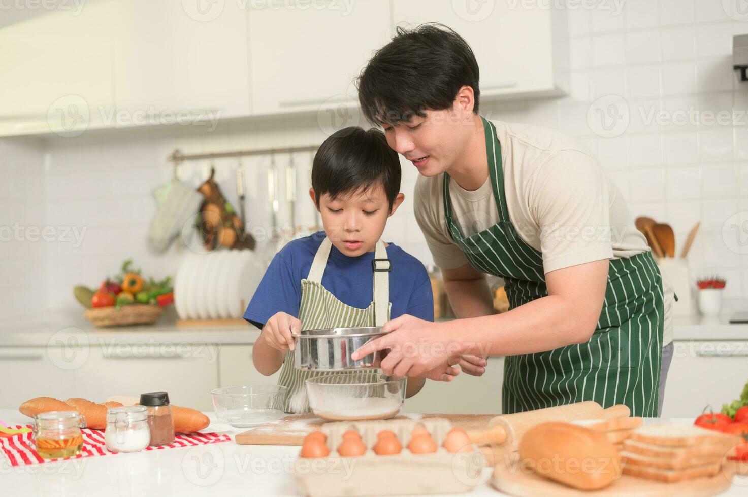 Lycklig ung asiatisk far och son matlagning i kök på Hem foto