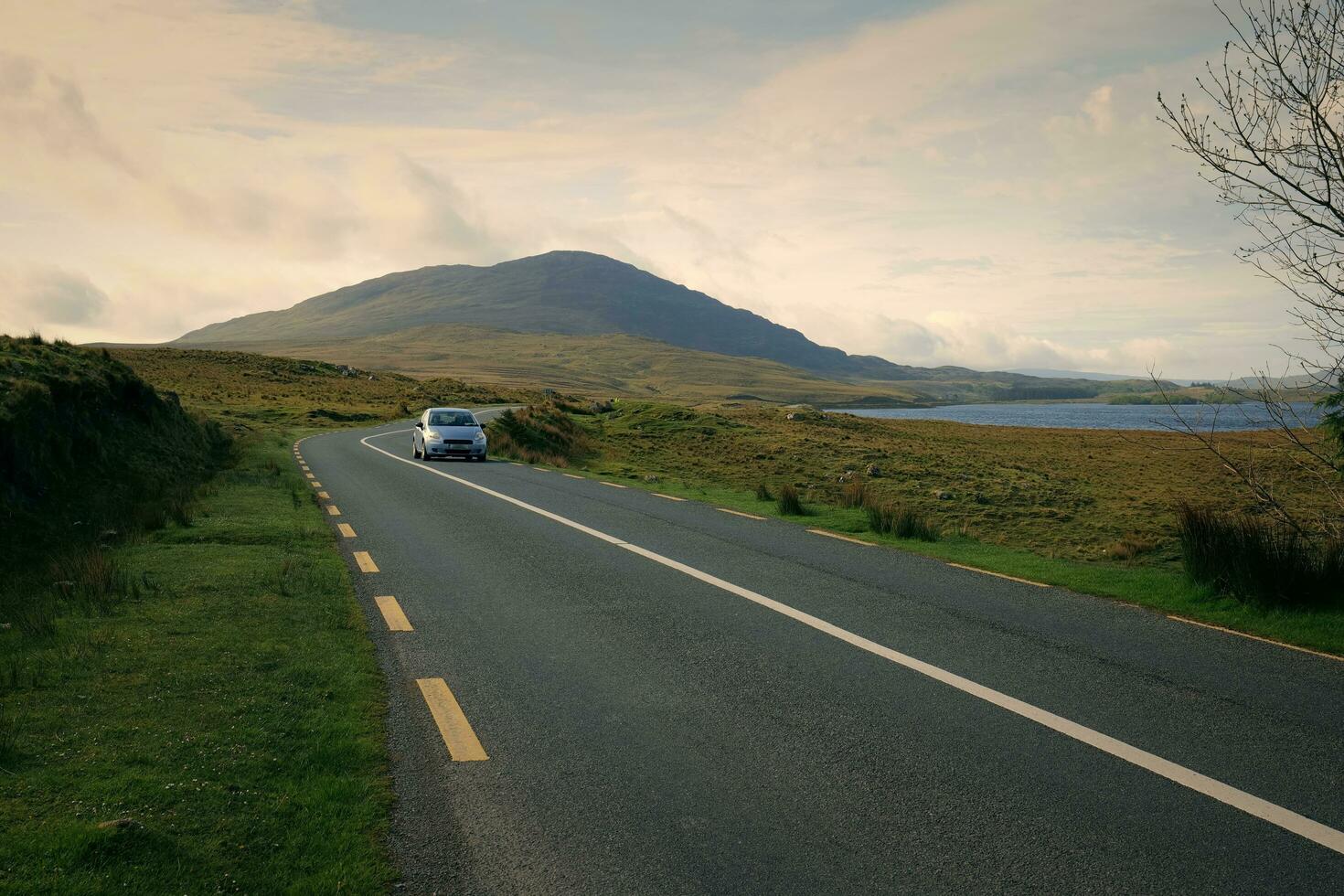 skön landskap landskap med bil körning på tömma naturskön väg tråg natur förbi de Lough inagh med bergen i de bakgrund på connemara nationell parkera i grevskap galway, irland foto