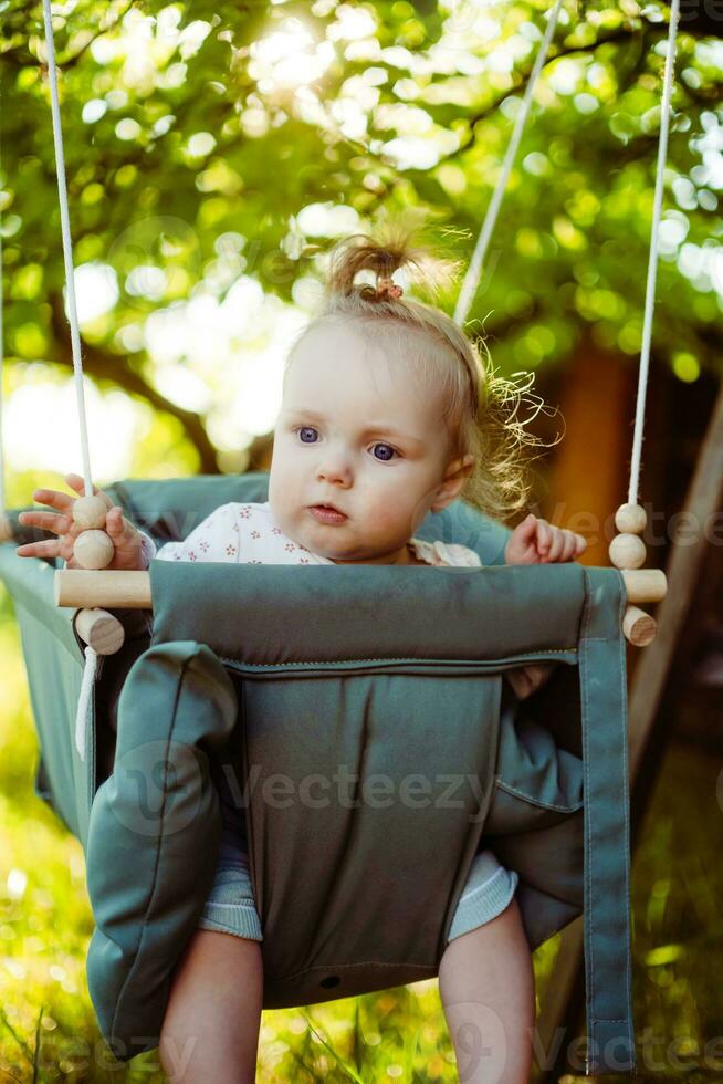 söt liten flicka i de gunga. bebis gunga på de träd i de trädgård. spädbarn spelar i de bakgård foto
