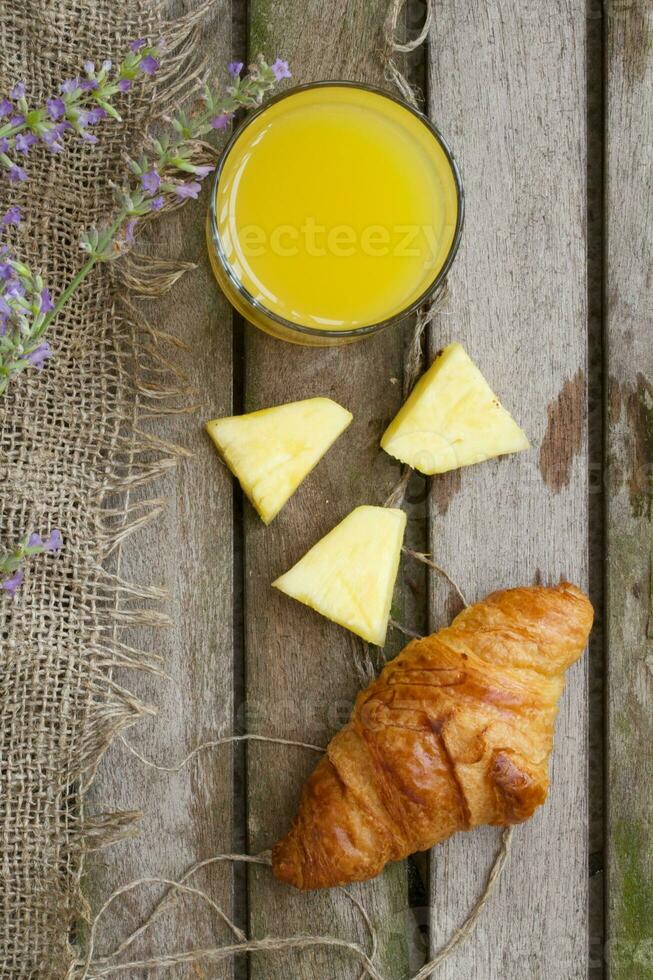 en glas av färsk ananas juice och en franska halvmåne rulla. bakgrund foto