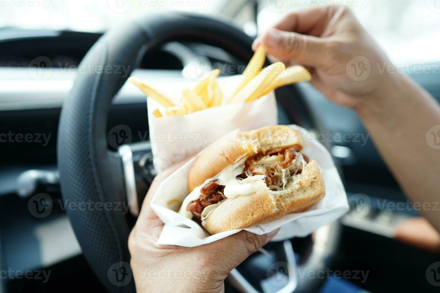 asiatisk kvinna förare håll och äta franska frites i bil, farlig och risk ett olycka. foto