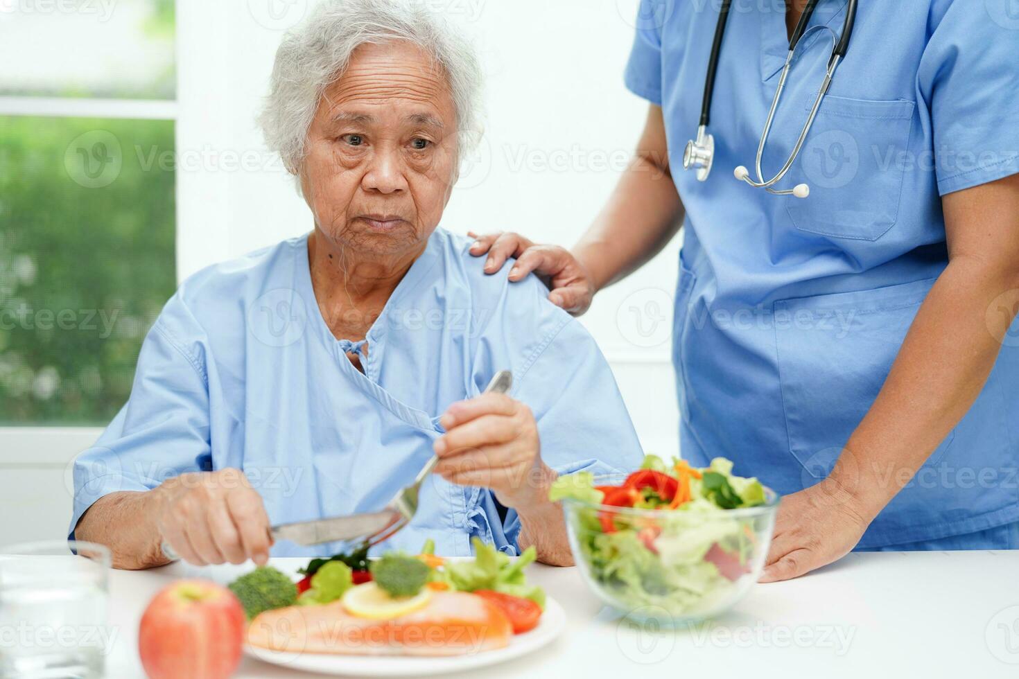 asiatisk äldre kvinna patient äter lax insats och vegetabiliska sallad för friska mat i sjukhus. foto