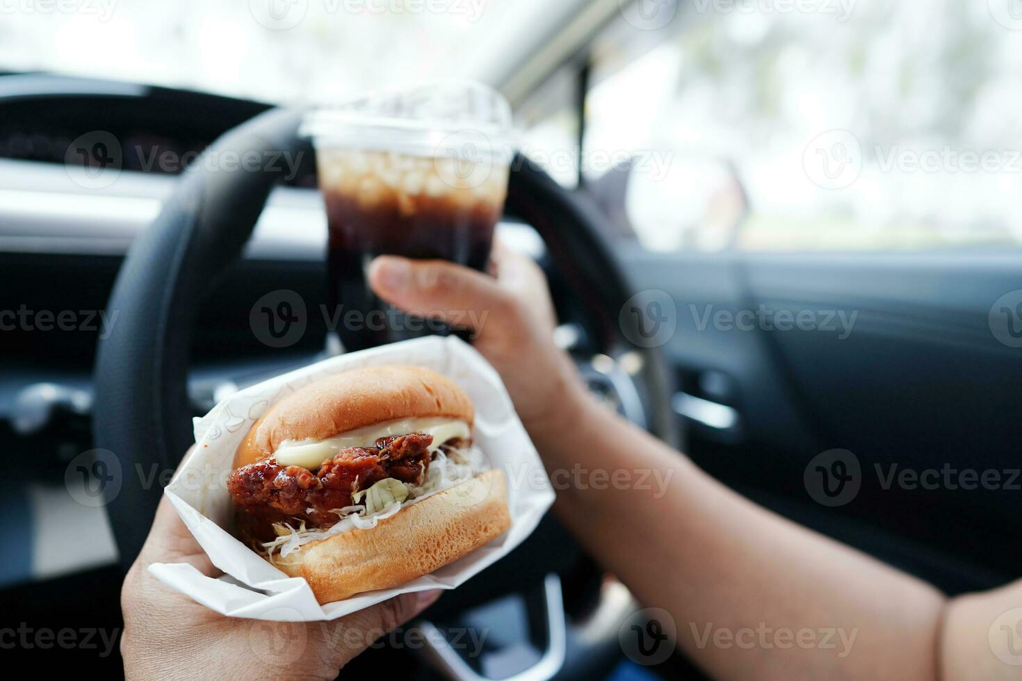 asiatisk kvinna förare håll och äta hamburgare i bil, farlig och risk ett olycka. foto