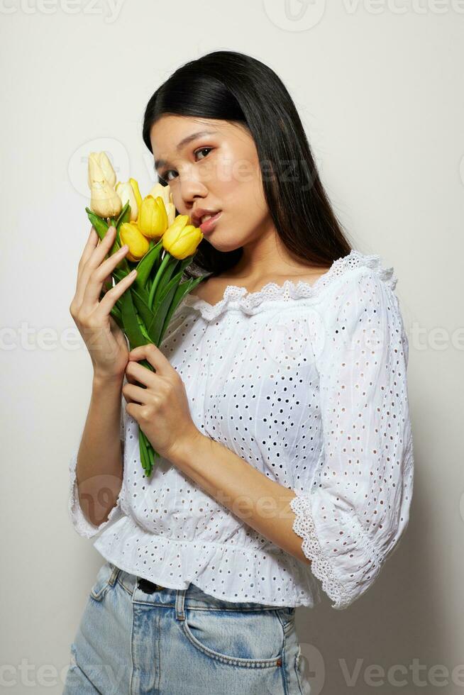 charmig ung asiatisk kvinna med en bukett av blommor leende närbild ljus bakgrund oförändrad foto