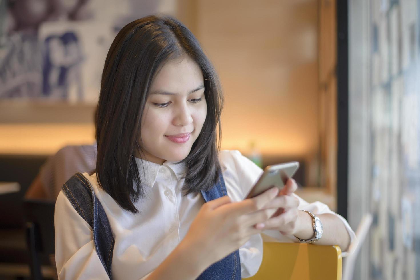 attraktiv kvinna som kontrollerar hennes meddelanden på smartphonen medan du sitter på kafé foto