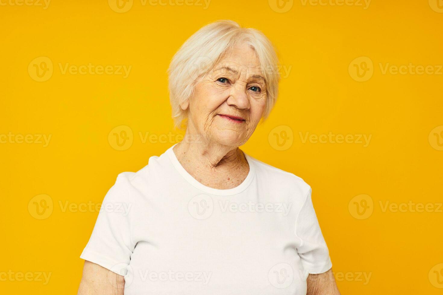 porträtt av ett gammal vänlig kvinna i vit t-shirt Framställ roligt gul bakgrund foto
