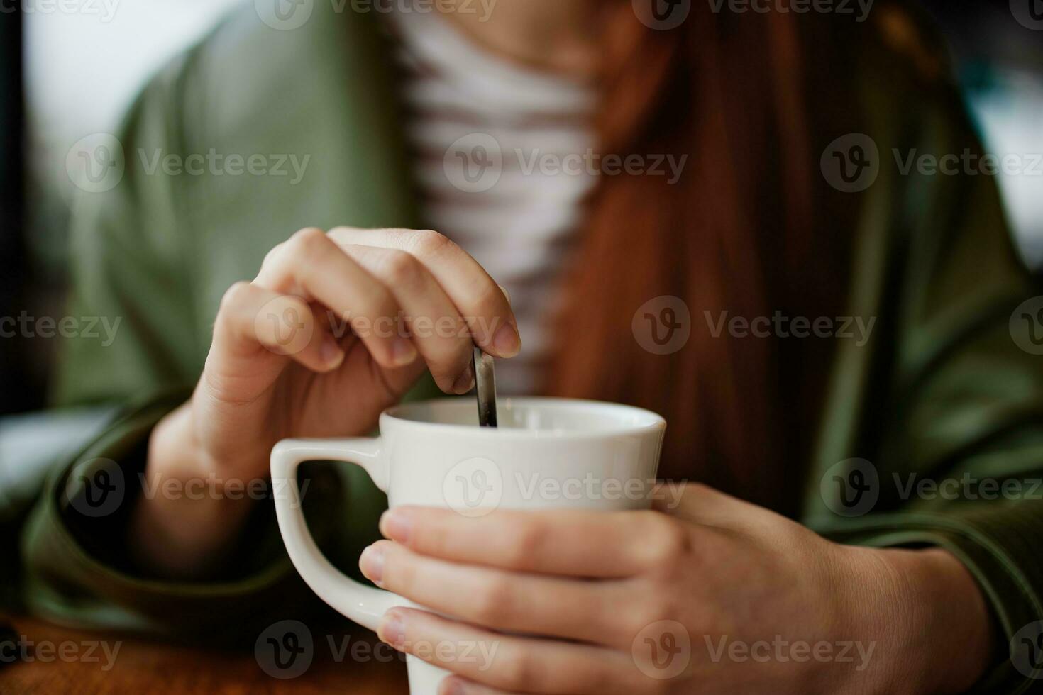 kvinna i Kafé omröring socker i vit kaffe mugg, höst atmosfär och värme foto