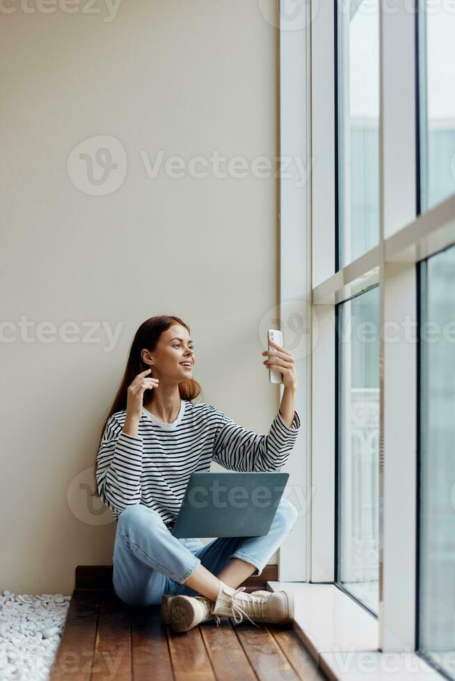 frilans kvinna Sammanträde med bärbar dator och telefon på fönster, video telefon ringa upp, lycka av arbete uppkopplad foto