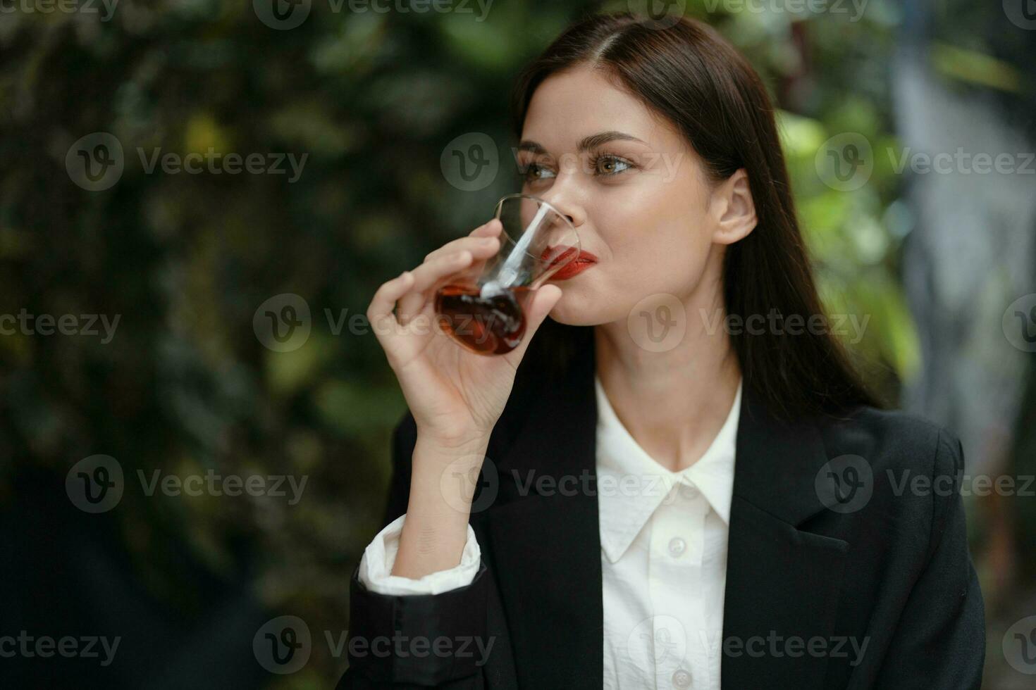 företag brunett kvinna med röd mun leende med tänder drycker te i en Kafé från en turkiska glas råna i en vit skjorta och svart mode jacka på de gata, sommar resa, semester i de stad foto
