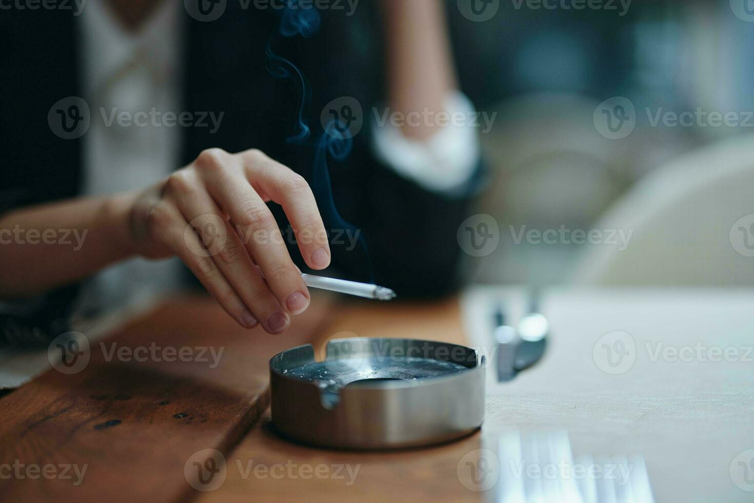 en kvinna med en cigarett i henne händer skakningar de aska in i ett askkopp, närbild foto