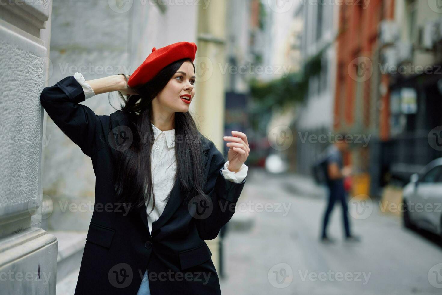 en kvinna stående nära en vägg i de stad bär en eleganta jacka och en röd basker med röd mun, reser. foto