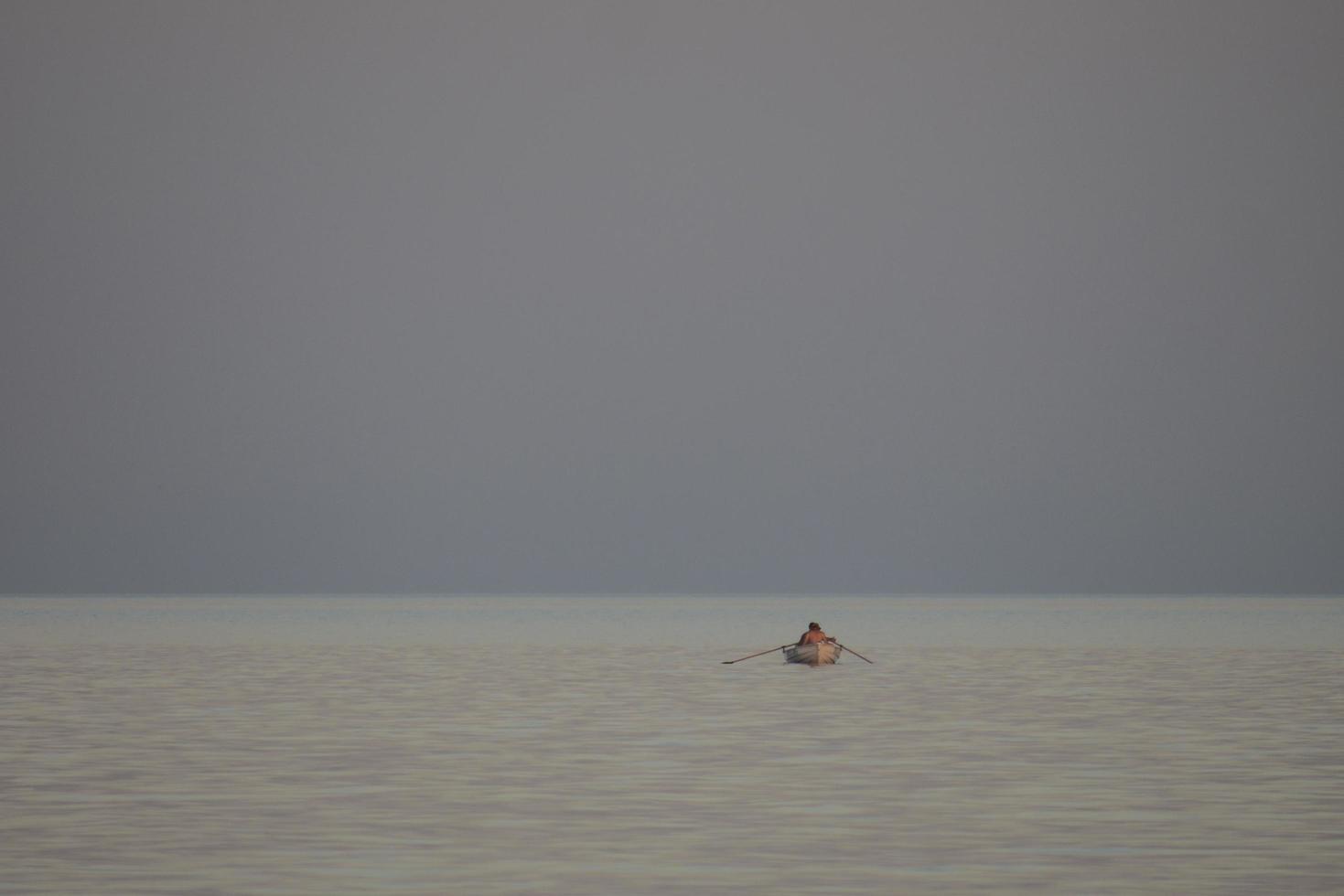 fiskare på en roddbåt i havet vid solnedgången foto
