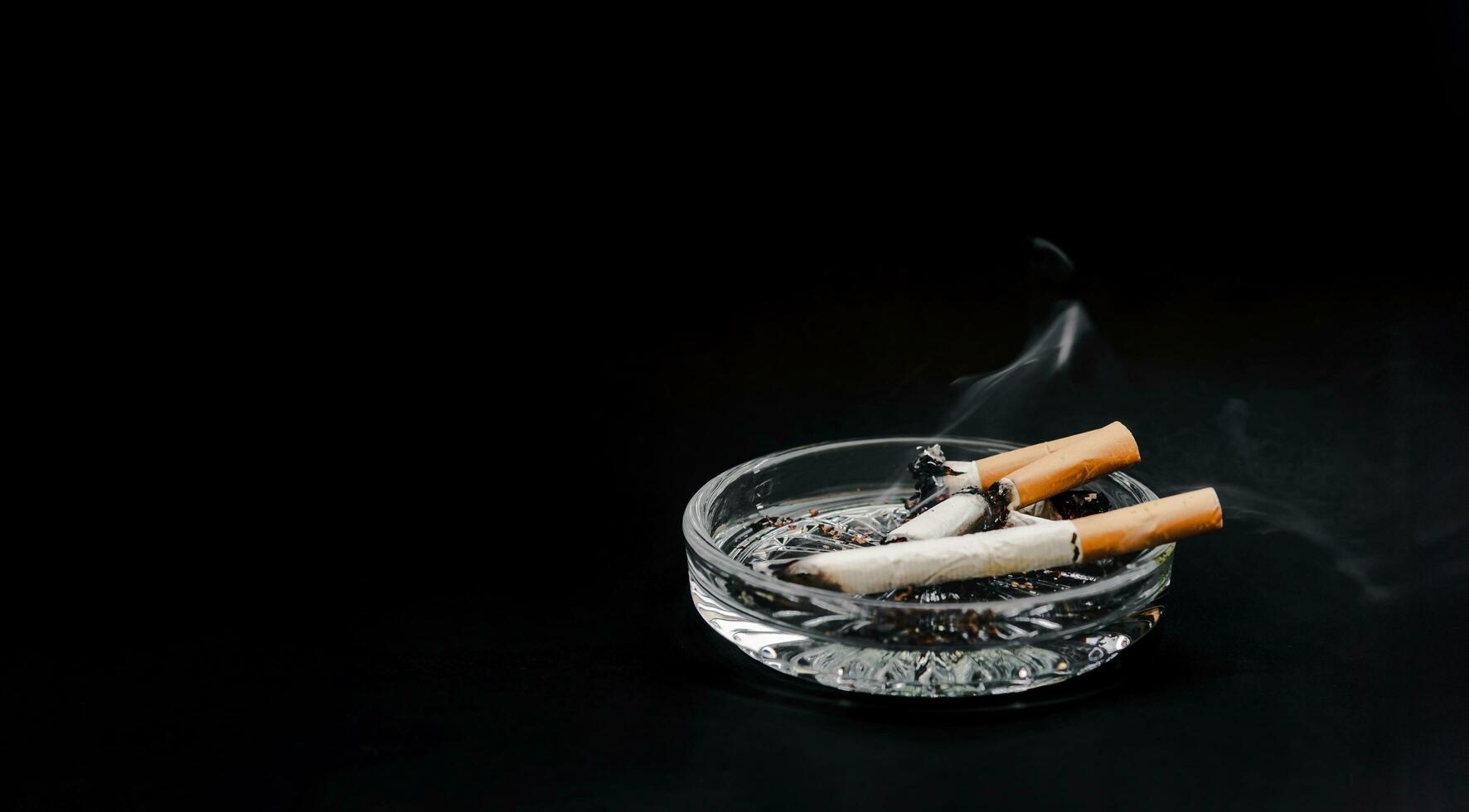 cigarett i de askkopp på en svart bakgrund. tobak, lunga cancer. foto