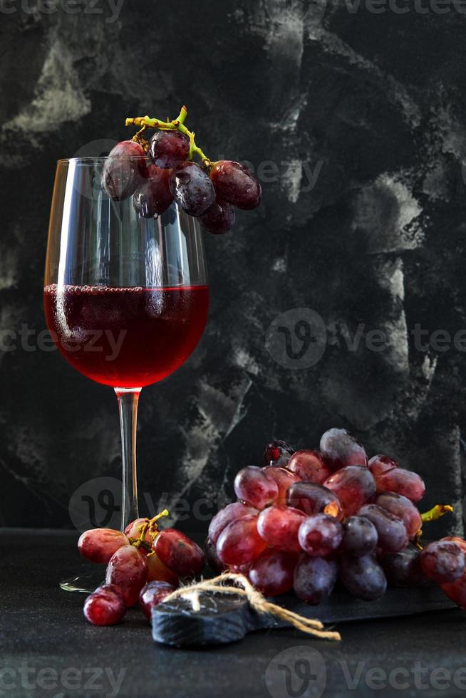 glas vin med druvor på ett svart träställ foto