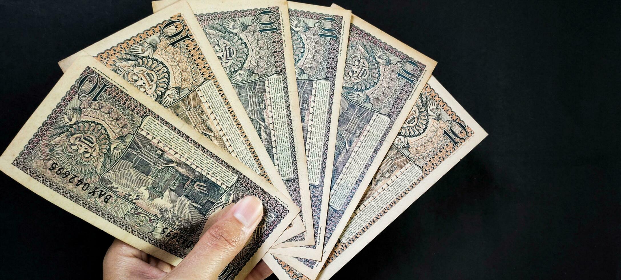 man innehav av gammal indonesiska sedlar rp.10,00 utfärdad i 1963. gammal rupiah valuta begrepp isolerat på en svart bakgrund. topp se foto