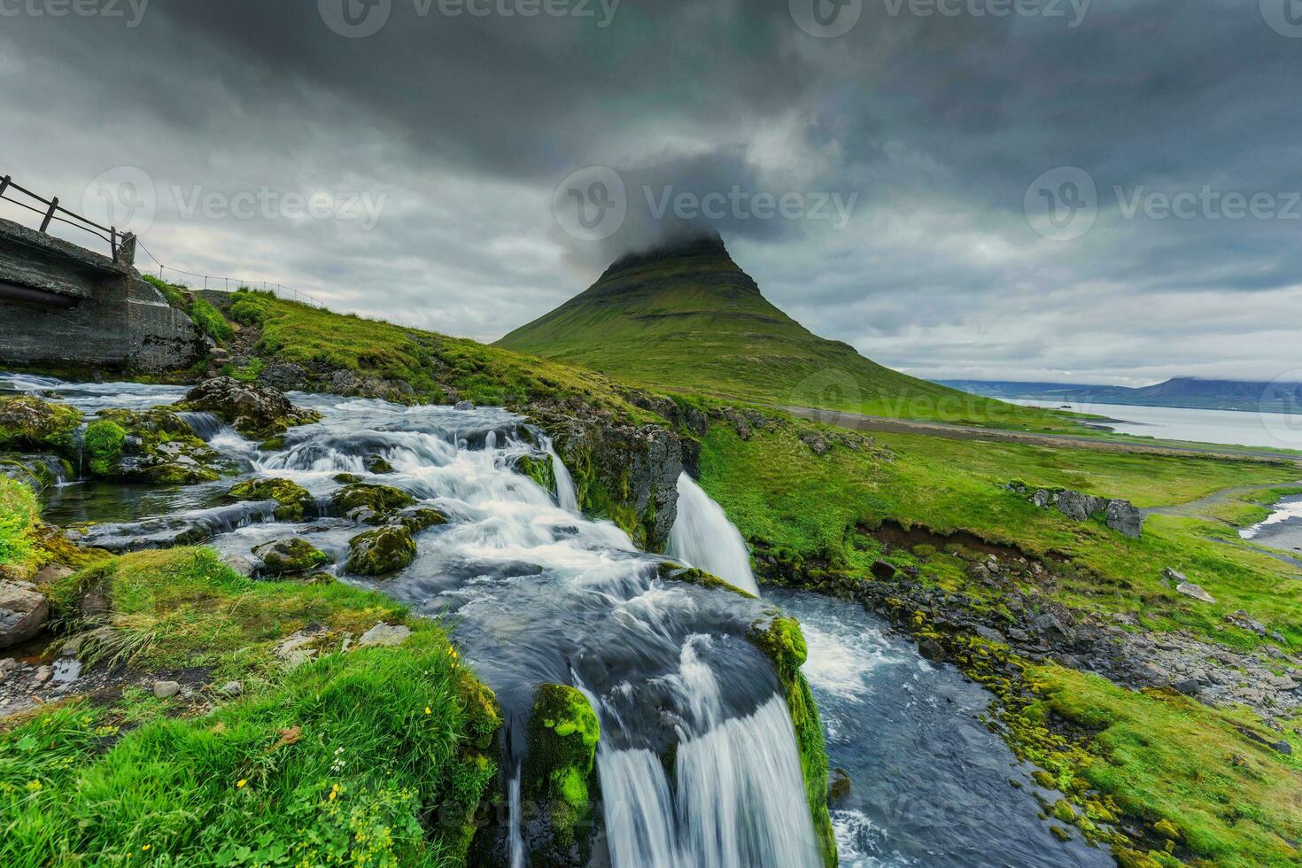 lynnig moln över Kirkjufell berg och vattenfall strömmande i sommar på island foto