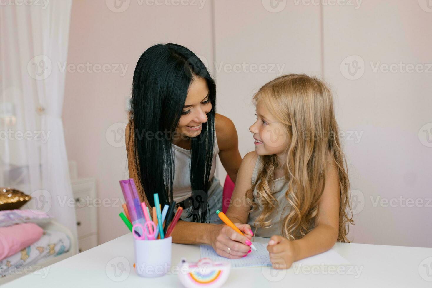 leende mor hjälper henne förtjusande dotter med läxa på rum foto