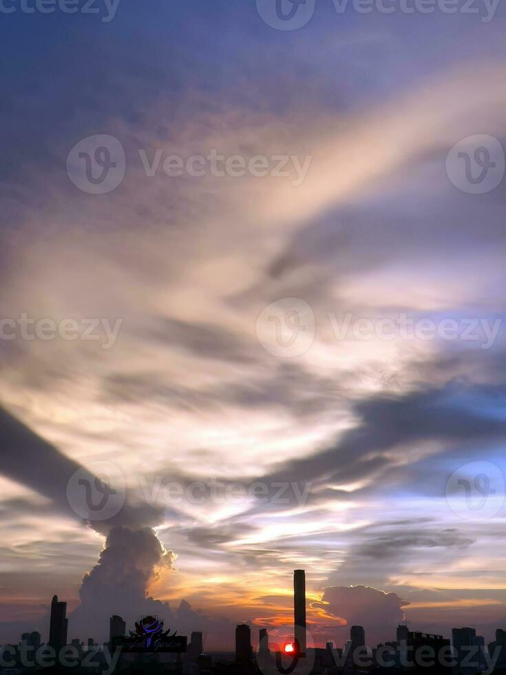 vertikal bild, solnedgång i de kväll med dramatisk form och Färg av moln och himmel med silhuett av stadsbild, byggnad horisont, natur bakgrund foto