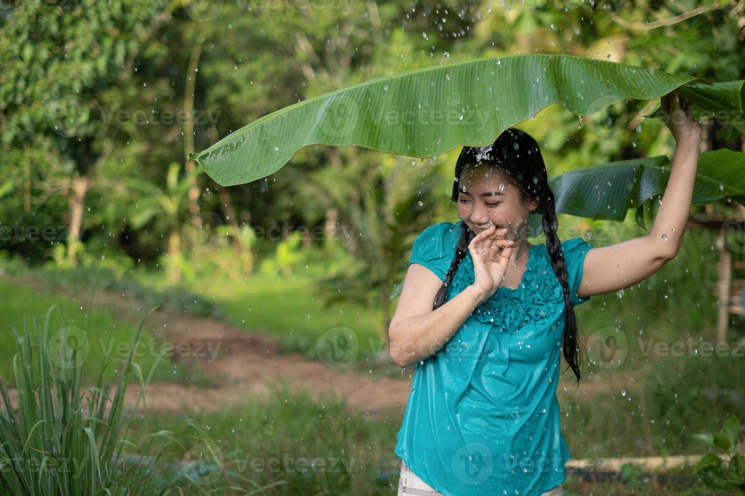 suddig bild porträtt av en ung asiatisk kvinna med svart hår som håller ett bananblad i regnet på den gröna trädgårdsbakgrunden foto