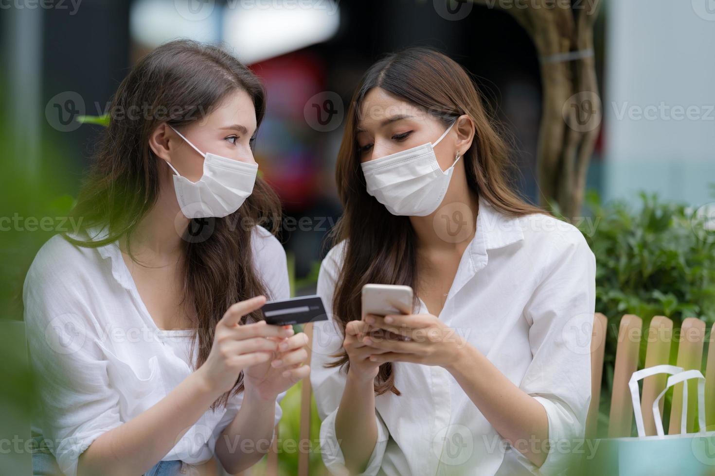 ung kvinna med bärande ansiktsmask skyddande prata och skratta håller kreditkort och använder telefon foto