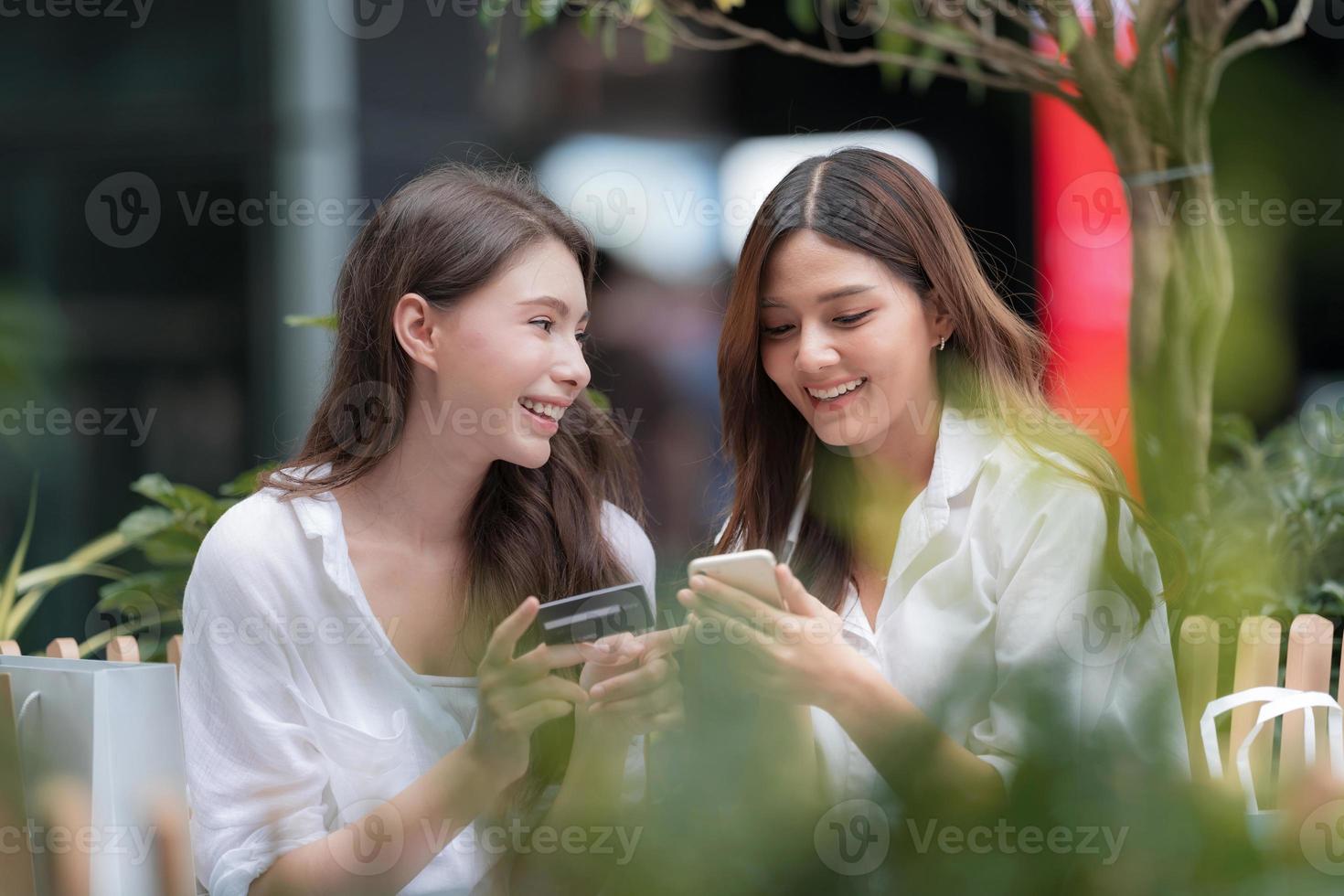 glad ung kvinna med smiley ansikte prata och skratta innehar kreditkort och använder telefon foto