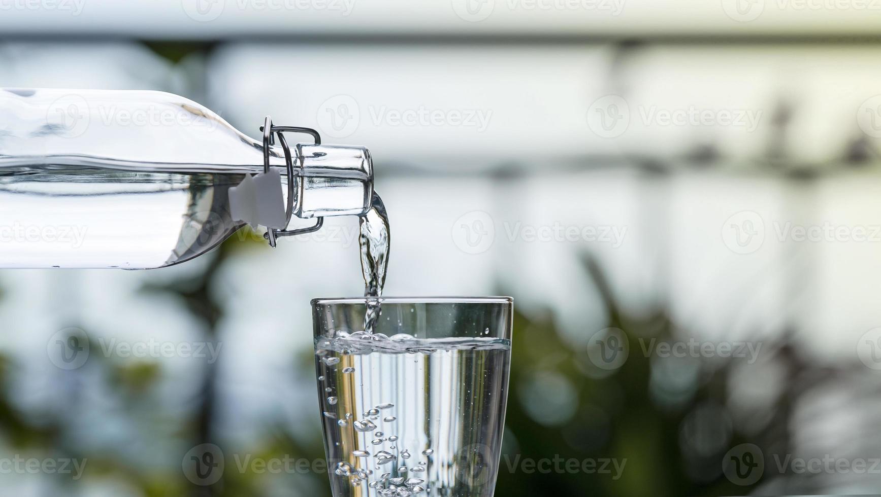 hälla dricksvatten från flaskan i glaset hemma i trädgården foto