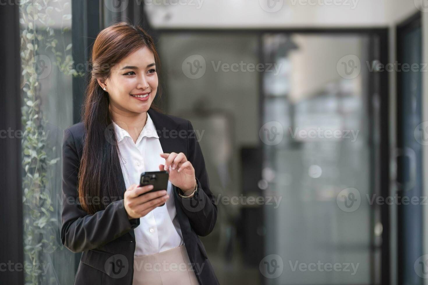 charmig asiatisk kvinna med ett leende som står och håller papper och mobiltelefon på kontoret. foto