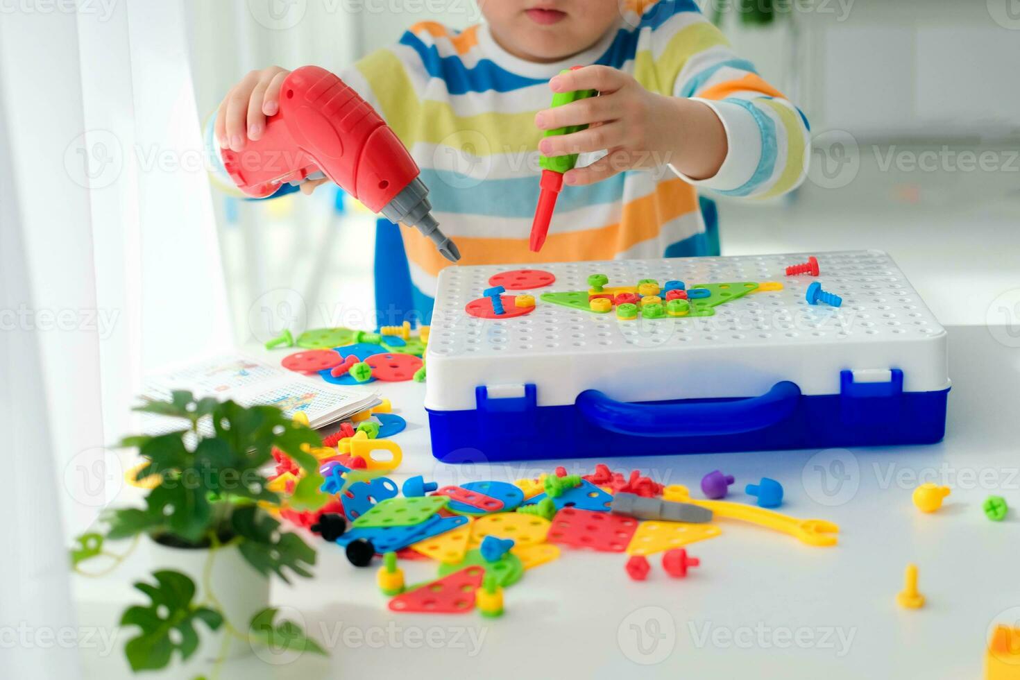 liten pojke spelar uppsättning med en skruvmejsel och en borra, och skruvar och delar . de barn spelar byggare med en leksak borra till utveckla fantasi och motor Kompetens. pedagogisk logik leksaker för barn. foto